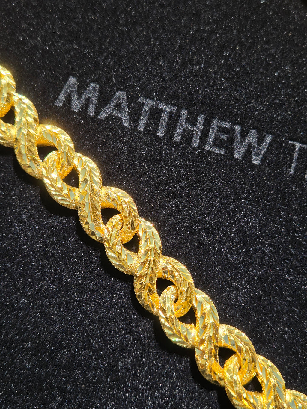 Solid gold infinity link chain showing the chevron diamond-cut facets stacked along each loop against frosted sandblasted passages