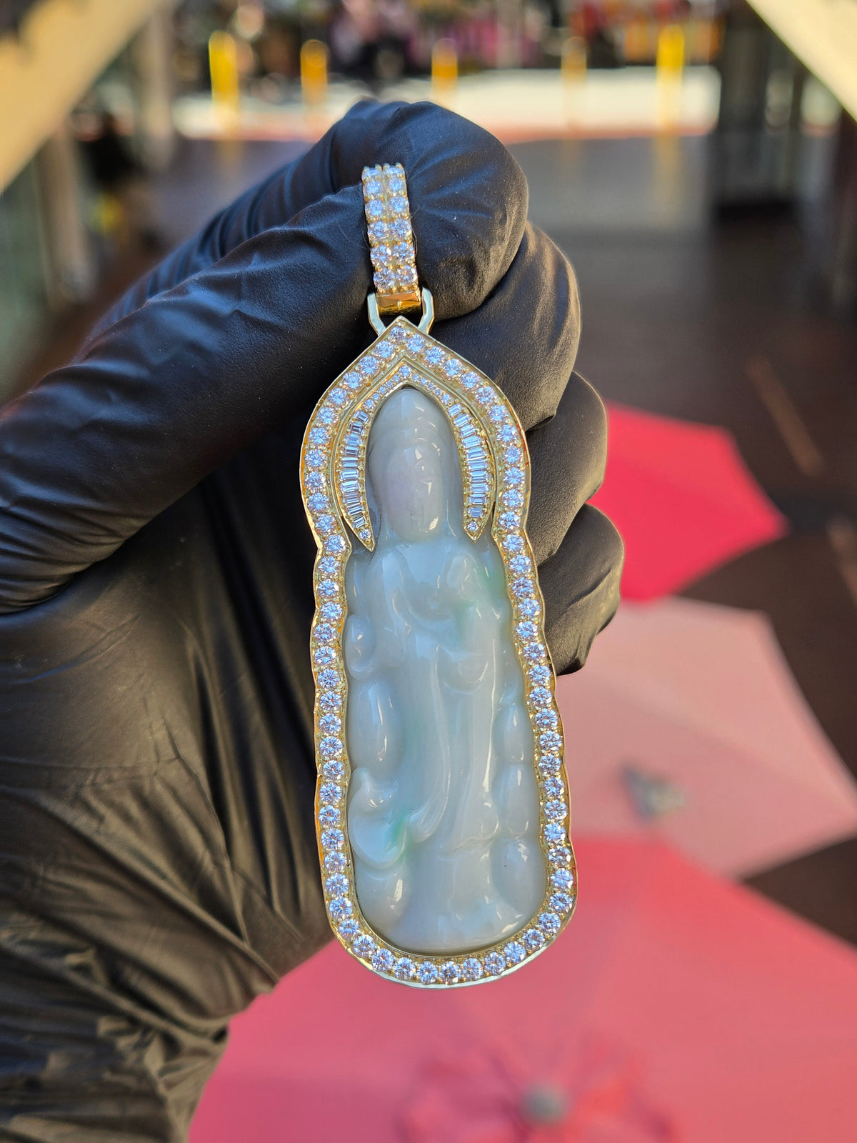 Jade Lady Buddha (Guan Yin) Round and Baguette Diamond Wrap Pendant in daylight, a carved jade plaque of Guan Yin standing on a lotus, framed in gold with round diamonds following the scalloped edge.