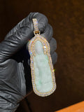 Front view of the Jade Lady Buddha (Guan Yin) pendant in warm indoor light, showing the channel-set baguette arch above the head and the green drifting through the carved jade.