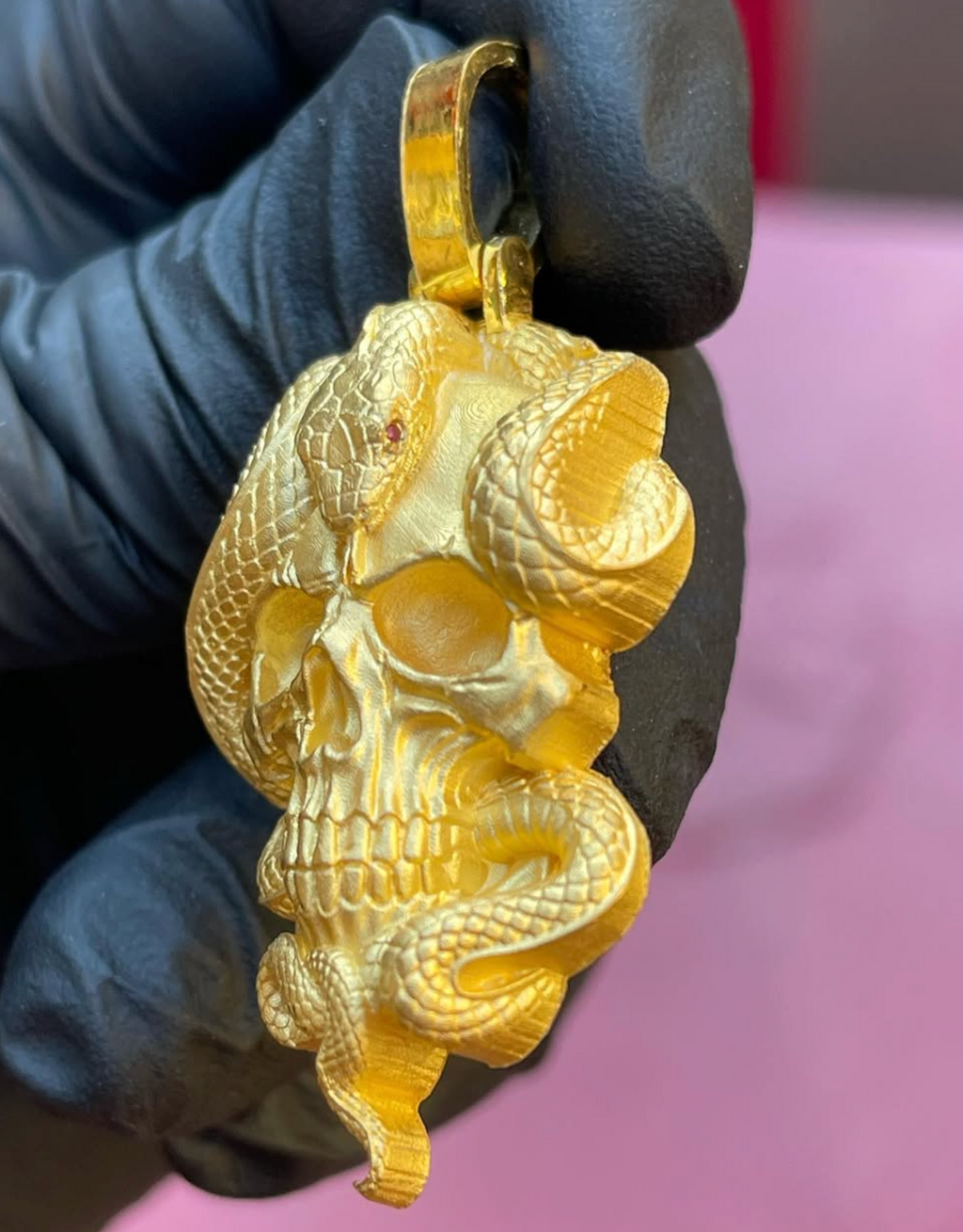 Skull and snake gold pendant, angled view showing the carved cranial suture and red stone snake eye