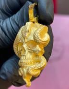 Skull and snake gold pendant, angled view showing the carved cranial suture and red stone snake eye