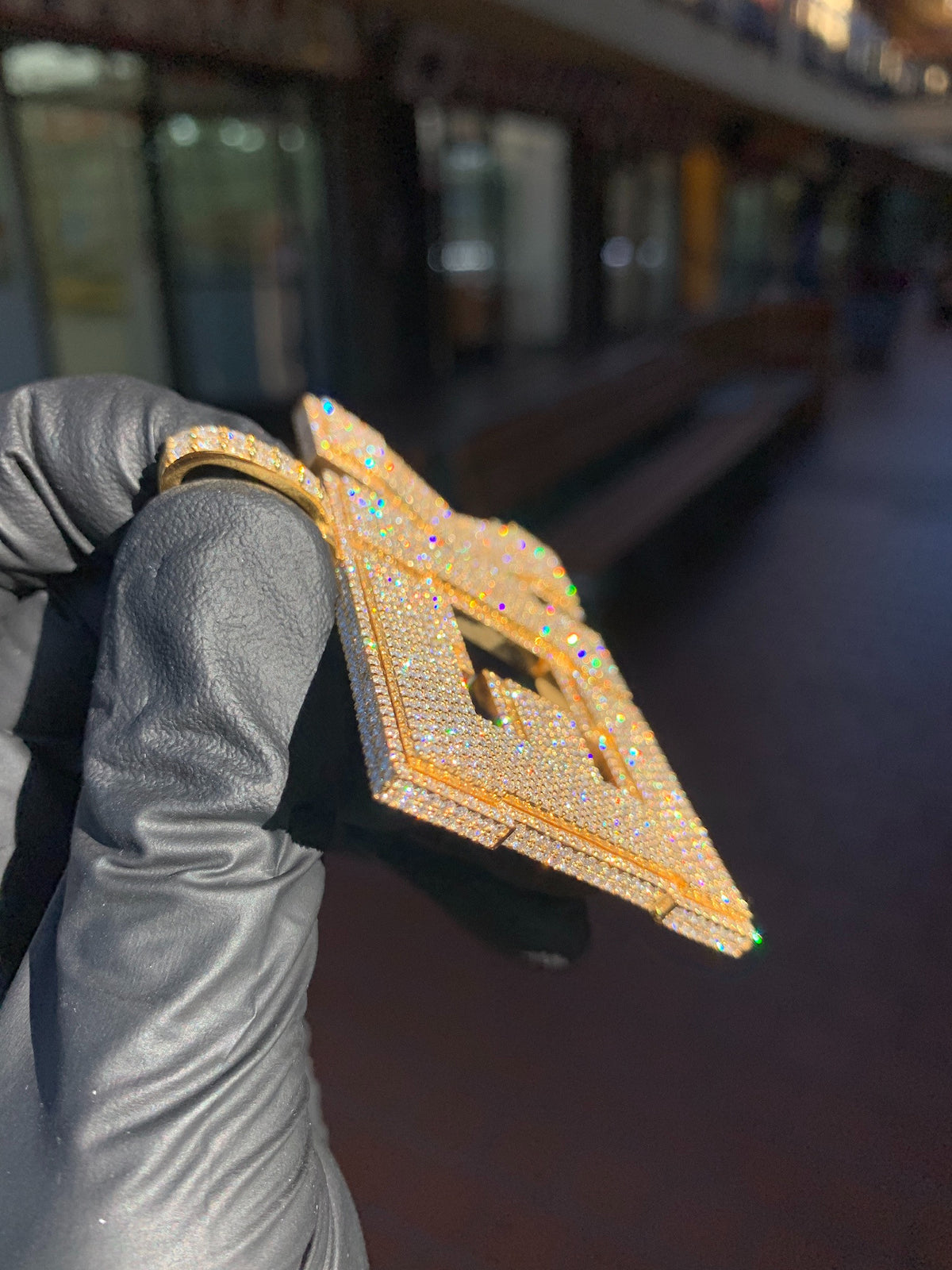 Angled view of the "EK" Diamond Pendant showing the stones carried over the top edge and the depth of the stepped border.
