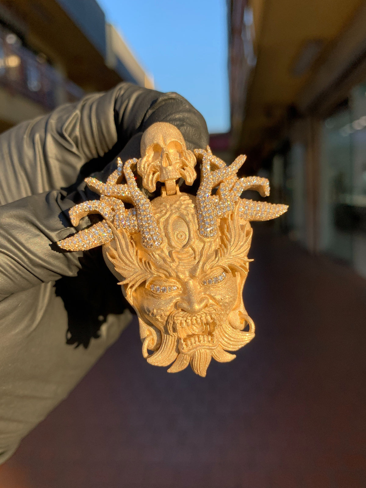 Yellow gold Japanese Oni Demon Mask Partial Diamond Pendant, a horned demon mask in satin gold with the horns, brows and third eye pave-set and a carved skull above.