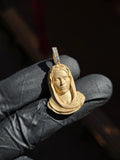 Small Virgin Mary Face gold pendant in sunlight, a sculpted bust with the head bowed and the veil falling in heavy folds