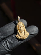 Small Virgin Mary Face gold pendant in sunlight, a sculpted bust with the head bowed and the veil falling in heavy folds