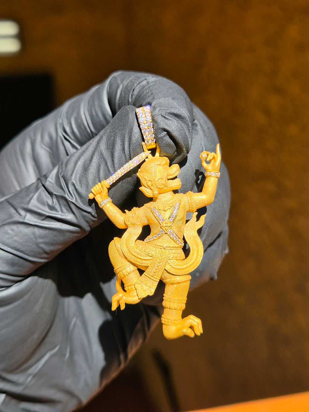 Thai Hanuman gold pendant in warm light, the monkey warrior mid-leap with a diamond-set staff raised over the crowned headdress